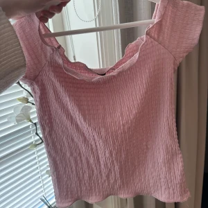 Rosa ribbad topp - Söt rosa ribbad topp med volangdetaljer vid halsringningen. Perfekt för en avslappnad och stilren look. Kortärmad design som passar bra till varmare dagar. Den är off shoulder!🥰Använd en gång!