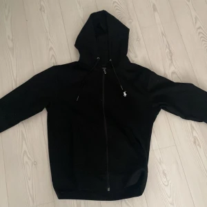 Svart hoodie från Ralph Lauren - Snygg svart hoodie från Ralph Lauren med dragkedja och broderad logga på bröstet. Perfekt för en casual look med sin bekväma passform och justerbara huva.