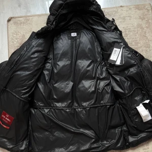 C.P Company DD Shell Puffer Jacket - C.P Company DD Shell Puffer Jacket  Color: Charcoal black Warmth: Suitable for cold weather, comfortable down to -25°C Closure: Zipper and button fastening Condition: 8.5/10 – Slight wear on the fabric (no down leakage), scratches on the lens Size: 48 – Fits M (can also work for L) Authenticity: CLG verified ✅PRICE: 200€