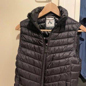Svart dunväst från McKinley - Säljer en svart dunväst från McKinley. Västen har en dragkedja framtill och är perfekt för kyligare dagar. Den är lätt och smidig att bära. Västen har inget tecken på användning och sitter perfekt för storlek 36