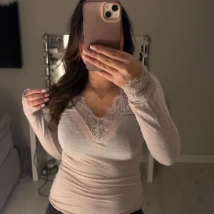 Beige långärmad topp med spetsdetaljer - Säljer en elegant beige långärmad topp med v-ringning och vackra spetsdetaljer vid hals och ärmslut. Perfekt för en stilren look. De är en M men passar för S också, är själv en S🤎🤍