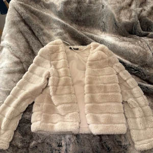 Beige teddyjacka från Gina Tricot - Mysig beige pälsjacka/kofta  från Gina Tricot. Jackan har en fluffig textur. och är perfekt för kyligare dagar. Passar båda inne och ute.