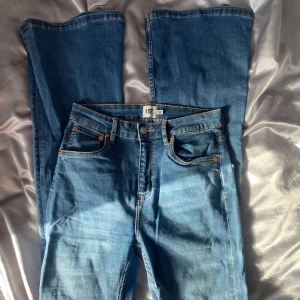 Blå jeans med bootcut - Snygga blå jeans med bootcut-stil och klassisk femficksdesign. De har en hög midja och är perfekta för en avslappnad look. Jeansen har en knapp och dragkedja framtill.