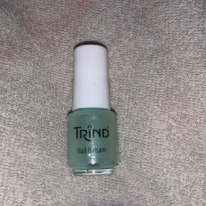 Trind Nail Balsam. Använd några gånger  - Trind Nail Balsam är en nagelvårdande produkt i en ljusgrön nyans. Den kommer i en liten glasflaska med en vit skruvkork och en inbyggd pensel för enkel applicering. Perfekt för att återfukta och stärka naglarna.