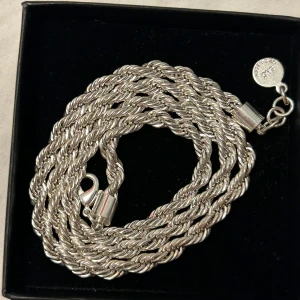 Silverfärgat halsband med tvinnad design - Snyggt silverfärgat halsband med en tvinnad design som ger en elegant look. Perfekt för att lyfta vilken outfit som helst. Den är cirka 50 cm. Har aldrig använts helt ny!