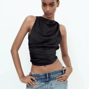 Svart topp med öppen rygg - Snygg svart  topp i satin med öppen rygg och knytning. Perfekt för en stilren och modern look. Helt ny, prislapp på. Orginalpris 299