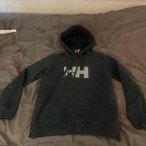 Mörkgrön hoodie från Helly Hansen - Säljer en snygg mörkgrön hoodie från Helly hansen. Tröjan är knappt använd och i storlek S. Hör av dig vid frågor!