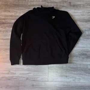 Svart hoodie från Gymshark - Säljer en stilren svart hoodie från Gymshark. Den har en klassisk design med långärmade ärmar och en praktisk huva. Det är i storlek S men sitter som en M-L helt ny   