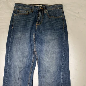 Blå jeans med läderdetalj - Snygga blå jeans med klassisk femficksdesign och en läderdetalj på baksidan. De har en dragkedja och knapp framtill. Perfekta för en avslappnad stil.