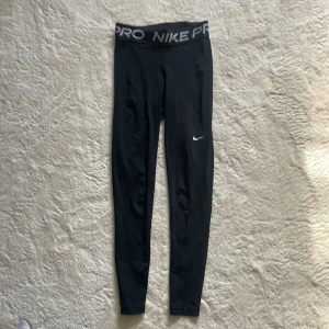 Svarta leggings från Nike - Snygga svarta leggings från Nike med hög midja och elastisk linning med Nike-logga. Perfekta för träning eller en aktiv vardag. Tillverkade i ett mjukt och stretchigt material för optimal komfort. Då de hade gått sönder där fram har jag sytt ihop de ( se bild 2)