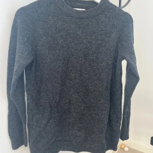 Grå stickad tröja i lammull - Säljer en mysig grå stickad tröja i lammull. Perfekt för kyliga dagar med sin klassiska design och långa ärmar. Tröjan har en rund halsringning och är gjord i en mjuk ullblandning.