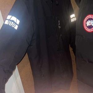 Svart jacka med reflexdetaljer - Säljer en svart jacka från Sail racing med reflexdetaljer på ärmarna och en broderad logotyp på bröstet. Jackan har en dragkedja framtill och är perfekt för kyligare väder.