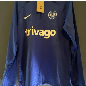 Blå Chelsea fotbollströja från Nike - Snygg blå Chelsea fotbollströja från Nike med lång ärm och klubbens logga på bröstet. Perfekt för fans som vill visa sitt stöd. Tröjan har även sponsorloggan 'trivago' tryckt på framsidan.