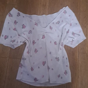 Vit blommig topp från Shein - Säljer en söt vit topp från Shein med blommigt mönster i rosa och grönt. Toppen har en offshoulder-design och korta ärmar, perfekt för sommarens varma dagar.