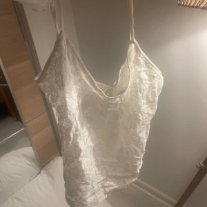 Vit spetslinne - Säljer ett vackert vitt spetslinne med tunna axelband. Linnet har ett blommigt mönster och en elegant design som passar perfekt för sommarens varma dagar. Står inte storlek men uppskattar till S/M❤️