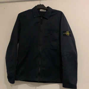 Navy  overshirt från Stone Island - Säljer en stilren navy  overshirt från Stone Island med dragkedja och ikonisk broderad logga på ärmen. Perfekt för lager-på-lager och en snygg casual look. Nypris ca 4000kr 