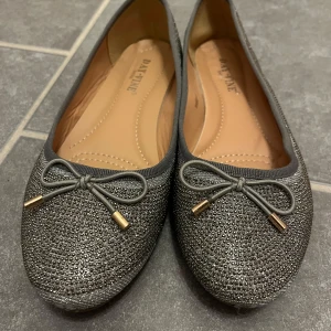 Glittriga ballerinaskor från Design by si  - Snygga glittriga ballerinaskor från Design by si i silver med dekorativa rosetter framtill. Perfekta för en utekväll. I nyskick bara använda 1 gång💓 storlek 38 skriv för mått