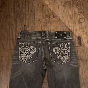 Grå bootcut jeans med broderade fickor - Snygga grå bootcut jeans från miss me med unika broderade mönster på bakfickorna. Jeansen har en cool tvättad look och detaljerade sömmar som ger dem en extra edge. Perfekta för dig som vill sticka ut! De är i storlek 30 men passar mig som vanligtvis har storlek 36 på jeans. De är väldigt lågmidjade och har en fin passform. Och dom är i väldigt bra skick. Pris kan diskuteras. Kom privat för bilder på/mått.