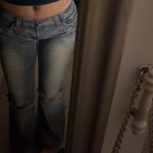Blå lågmidjade bootcut jeans med broderad detalj - Snygga lågmidjade blå vintage jeans med slitna detaljer och en cool broderad 'cheerleader'-design på bakfickan. Passar dig som är 158-162 lång. Är en 34-36 i storleken skulle jag säga. Märket är okänt.