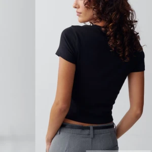 Svart croppad t-shirt - Snygg svart croppad t-shirt med korta ärmar. Perfekt för en stilren och avslappnad look. Har knappt kommit till användning. 