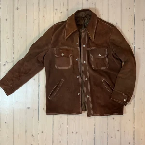Brun mockajacka, cowboys stil! - Vintage mockajacka – cowboystil i toppklass!  Säljer en mycket fin vintagejacka i brun mocka med tydlig cowboystil. Perfekt för både höst och vår!    •   Design: Robust och kraftig jacka med vita kontrastsömmar, snygga lock och flera praktiska fickor.    •   Stil: Passar lika bra på stan som för en skogspromenad eller en tur till häst.    •   Komfort: Riktigt skön att bära och gjord i högkvalitativ mocka för lång hållbarhet.  En unik jacka som sticker ut med sin coola look och funktionalitet. 