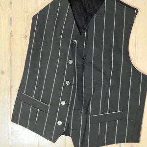 Svart randig väst med byxor oxh skjorta med krås från Bill Tornade - Snygg svart väst å byxor med vita ränder från Bill Tornade. En benvit otroligt fin skjorta i krås tillkommer om man vill köpa till den för full Prince uniform :) Unik design från tidigt 90-tal, inköpt på JUS Brunnsgatan 7. www.jus.se Västen och byxorna har en klassisk design med knappar framtill och två fickor. Perfekt för en stilren look. Du hittar inga sådana här kläder idag! Lagom för långsmal kille eller tjej mellan 173-177, ca. 29-30 i midja