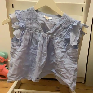 Ljusblå blus från Gina Tricot - Söt ljusblå blus från Gina Tricot med volangdetaljer vid ärmarna och v-ringning. Perfekt för varmare dagar och ger en luftig känsla. Lite skrynklig men går att stryka, säljer pga storlek 