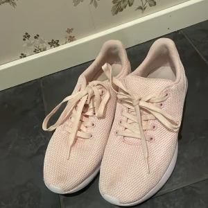 Ljusrosa sneakers med snörning - Säljer ett par ljusrosa sneakers med snörning. Skorna har en stilren design med en stickad ovandel och en vit sula. Perfekta för en avslappnad stil och gympa skor.