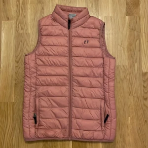 Rosa dunväst från Hangten - Säljer en snygg rosa dunväst från Hangten. Västen har en dragkedja framtill och en hög krage för extra värme. Perfekt för kyliga dagar och lätt att matcha med olika outfits.