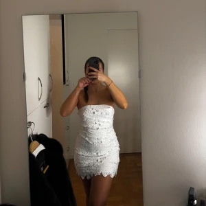 Vit axelbandslös klänning - Säljer denna otroligt fina och söta axelbandslösa klänningen med blommig brodyr. Aldrig använd och är i super skick! Kan användas både som mini samt mid klänning. Passar perfekt som bl.a. studentklänning!