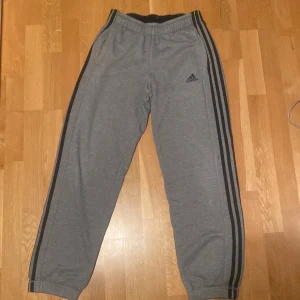 Grå mjukisbyxor från Adidas - Säljer ett par grå mjukisbyxor från Adidas. Byxorna har en elastisk midja och är perfekta för en avslappnad stil. Har vissa färg fläckar lite under knäna och på den bakre delen. Skick 6/10