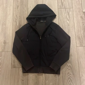 Svart hoodie från Polo Ralph Lauren - Säljer en stilren navy blue hoodie från Polo Ralph Lauren. Skick 7/10, den sömmen har gått upp på ena ärmen. Storleken på cardiganen är S. Nypriset är 2000kr. Priset kan diskuteras.