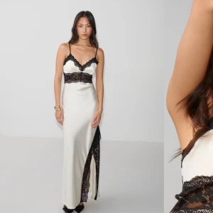 Vit långklänning med svart spets - Elegant vit långklänning med svarta spetsdetaljer och smala axelband. Klänningen har en slits och v-ringad design med spets som ger en sofistikerad look. Köpt för 700kr helt oanvänd med prislapp kvar. Snabb affär 550kr