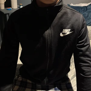 Svart jacka från Nike - Säljer en svart jacka från Nike med dragkedja och hög krage. Jackan har långa ärmar och en vit Nike-logga på bröstet. 