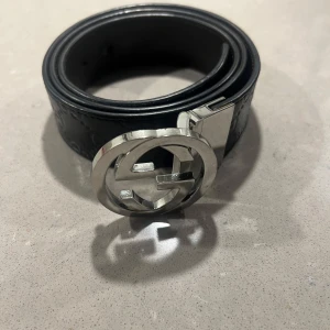 Svart skärp med silverfärgat spänne - Snyggt svart skärp med ett iögonfallande silverfärgat spänne. Skärpet har ett diskret mönster och är perfekt för att ge en stilren touch till din outfit.