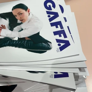 GAFFA Magasin - En hög med GAFFA magasin med en person i vit skjorta och svarta byxor på omslaget. Magasinet har en modern design med blå text och är staplade i en hög.