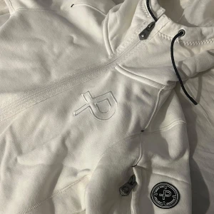 Vit hoodie från Pelle P - Säljer en stilren vit hoodie från Pelle P med dragkedja och justerbar huva. Storlek xs en liten detalj som finns på en av bilderna att det finns en liten fläck som jag inte fick bort o tvätten men den går nog bort efter några tvättar till. Nypris 1400:- 
