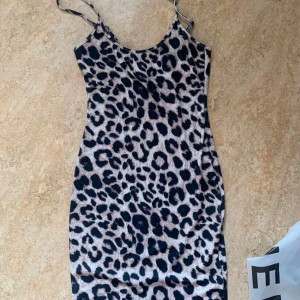 Leopardmönstrad klänning med smala axelband - Trendig leopardmönstrad klänning med smala axelband. Perfekt för en djärv look. Klänningen har en figurnära passform och är tillverkad i ett mjukt material.