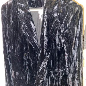 Svart sammet kavaj från Gina Tricot - Elegant svart kavaj i sammet från Gina Tricot. Kavajen har en klassisk design med knappar framtill och en glansig yta som ger en lyxig känsla. Perfekt för att höja stilen på vilken outfit som helst.