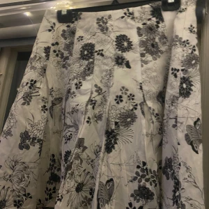 Blommig kjol från KappAhl - Säljer en superfin blommig kjol från KappAhl i storlek 40. Kjolen har ett vackert svartvitt blommönster som ger en elegant touch. Perfekt för både vardag och fest! 🌸