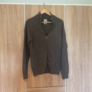 Dobber fullzip kofta - Säljer en snygg grå kofta med dragkedja framtill. Perfekt för höst och vinter, den är både stilren och bekväm. Koftan har långa ärmar och ribbade kanter vid ärmslut och nederkant. Nästan aldrig använd den är i perfekt skick!