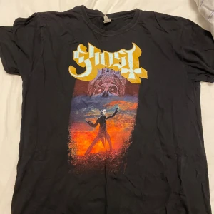 Svart Ghost t-shirt med tryck - Säljer en svart t-shirt med ett coolt tryck från bandet Ghost. Denna är väl använd men syns inte alls, det står XXL i storlek men passar mig jättebra som har M