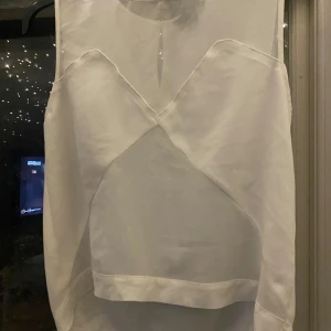 Vit topp från H&M - Säljer en stilren vit topp från H&M i storlek S. Toppen har en unik design med en öppen rygg och är ärmlös, vilket gör den perfekt för både vardag och fest. Materialet känns mjukt och skönt mot huden.