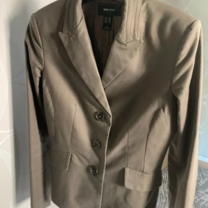 Beige kavaj från H&M - Säljer en stilren beige kavaj från mng suit i storlek 38. Kavajen har en klassisk design med knappar framtill och fickor. Perfekt för både vardag och fest!