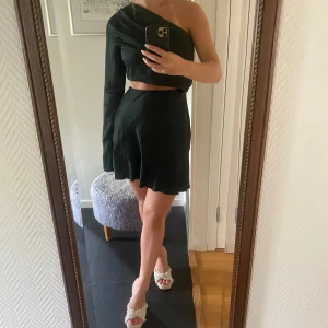 Ahlvar Gallery klänning  - Mörkgrön asymetrisk klänning i glansigt tyg från Aglvar Gallery. Storlek XS. Resår i midjan på ”kjolen”. Använd 1 gång. Klänningen ger intryck av ett matchande set med kjol och topp (dessa sitter ihop på ena sidan). Nypris ca 2000kr🩷