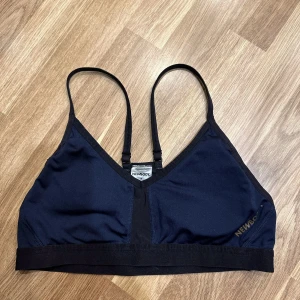 Svart sport-bh från Newbody - En svart/blå sport-bh från Newbody. Den är i ett mjukt och stretchigt material, perfekt för träning. Bh:n har smala axelband och en enkel design utan onödiga detaljer. Passar bra för både låg- och medelintensiva aktiviteter. Storlek M
