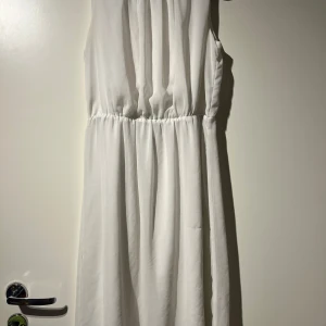 Vit ärmlös klänning - Säljer en elegant vit ärmlös klänning. Den har en enkel och stilren design med en elastisk midja som ger en fin passform. Perfekt för sommarens fester eller en avslappnad dag ute.