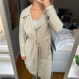 Beige trenchcoat DDP Maison fondée en 1985  - Fin beige trenchcoat från märket ”DDP Maison fondée en 1985”. Den har ett liten fläck på ryggen, men inget man lägger märke till (går hundra procent bort i tvätten). Storlek Small.