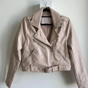 Beige skinnjacka från Pull&Bear - Säljer en snygg beige skinnjacka från Pull&Bear. Den har en cool bikerstil med dragkedjor och ett bälte i midjan. Jackan är långärmad och perfekt för höst och vår. Den är i bra skick och redo för nya äventyr!