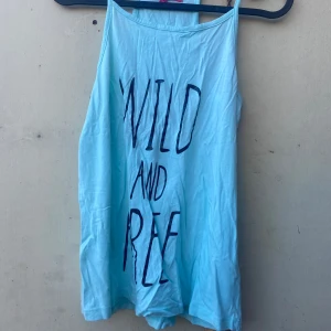 Ljusblå linne från Still Summer Vibes - Säljer ett superhärligt ljusblått linne från Still Summer Vibes. Perfekt för sommardagar med texten 'Wild and Free' tryckt på framsidan. Linnet är ärmlöst och har en avslappnad passform. Perfekt för stranden eller en dag i parken!